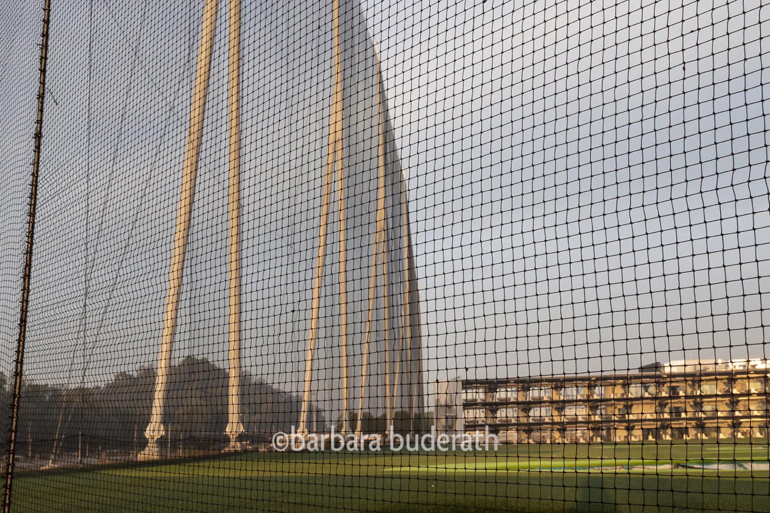 Fotografie: Sportanlage Topgolf in Oberhausen . Man sieht auf das Abschlagsgebäude. Fotografiert durch das Sicherungsnetz.