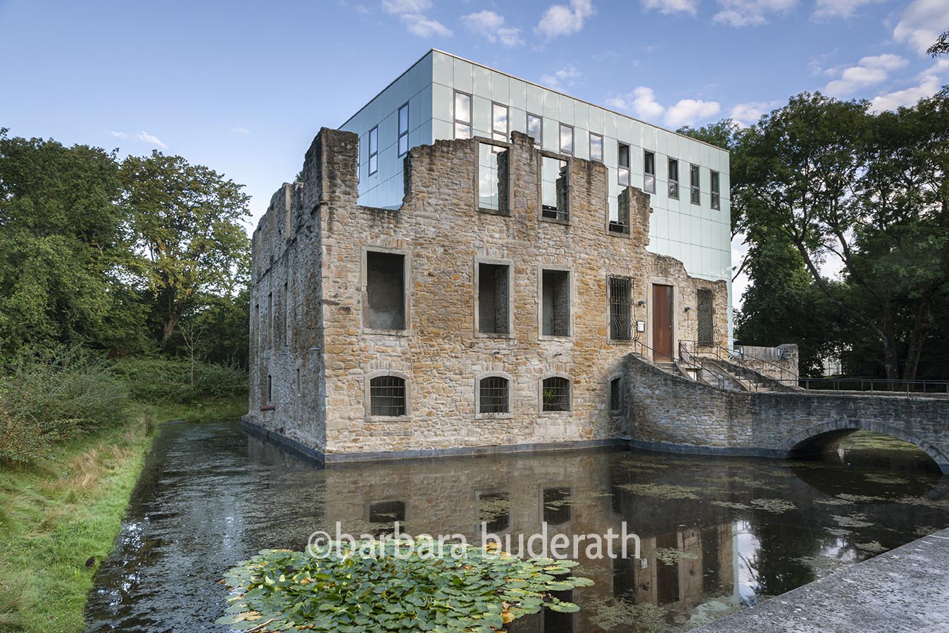 Fotoaufnahme von Haus Weitmar in Bochum mit Burggraben und Brücke. Im Vordergund Seerosenblätter