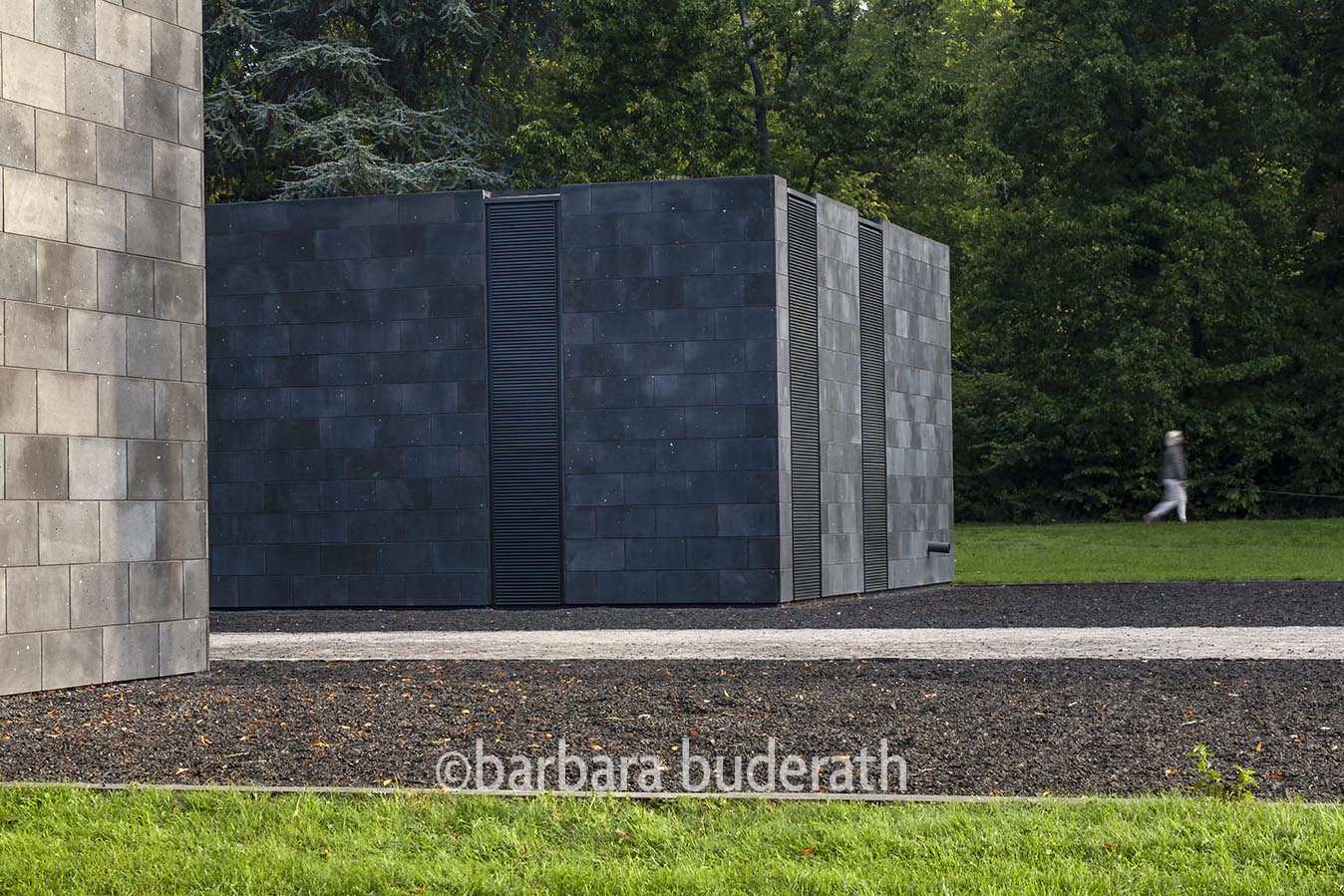 Aussenarchitekturaufnahme des Museums unter Tage mit einer Frau die im Hintergrund durch den Park läuft