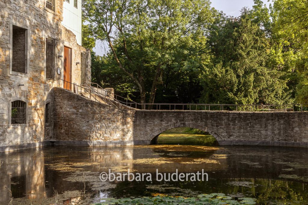 Blick auf die Brücke aus Natursteinen über den Wassergraben von Haus Weimar in Bochum